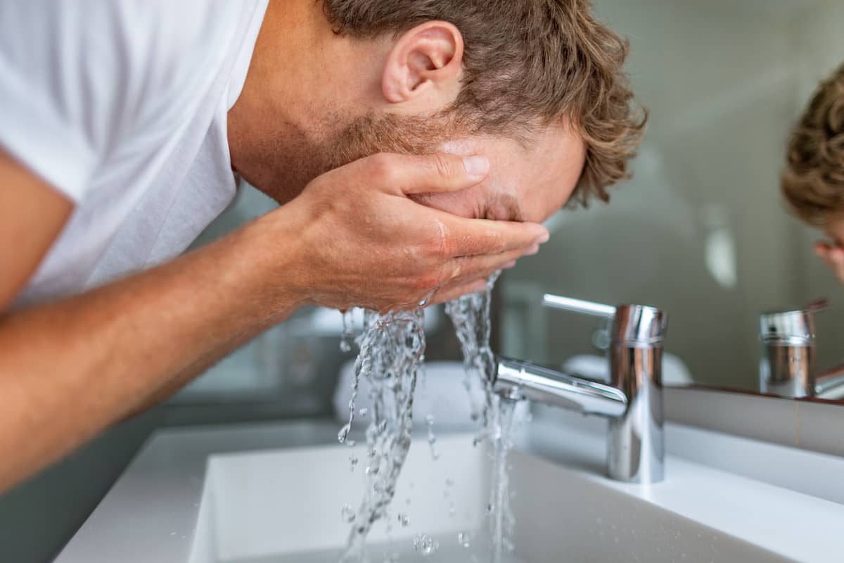 Mann wäscht sich das Gesicht mit den Händen