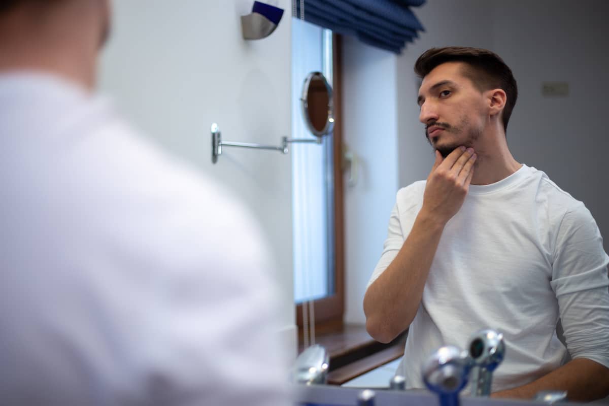 Mann mit dünnem Bart sieht sich im Spiegel an
