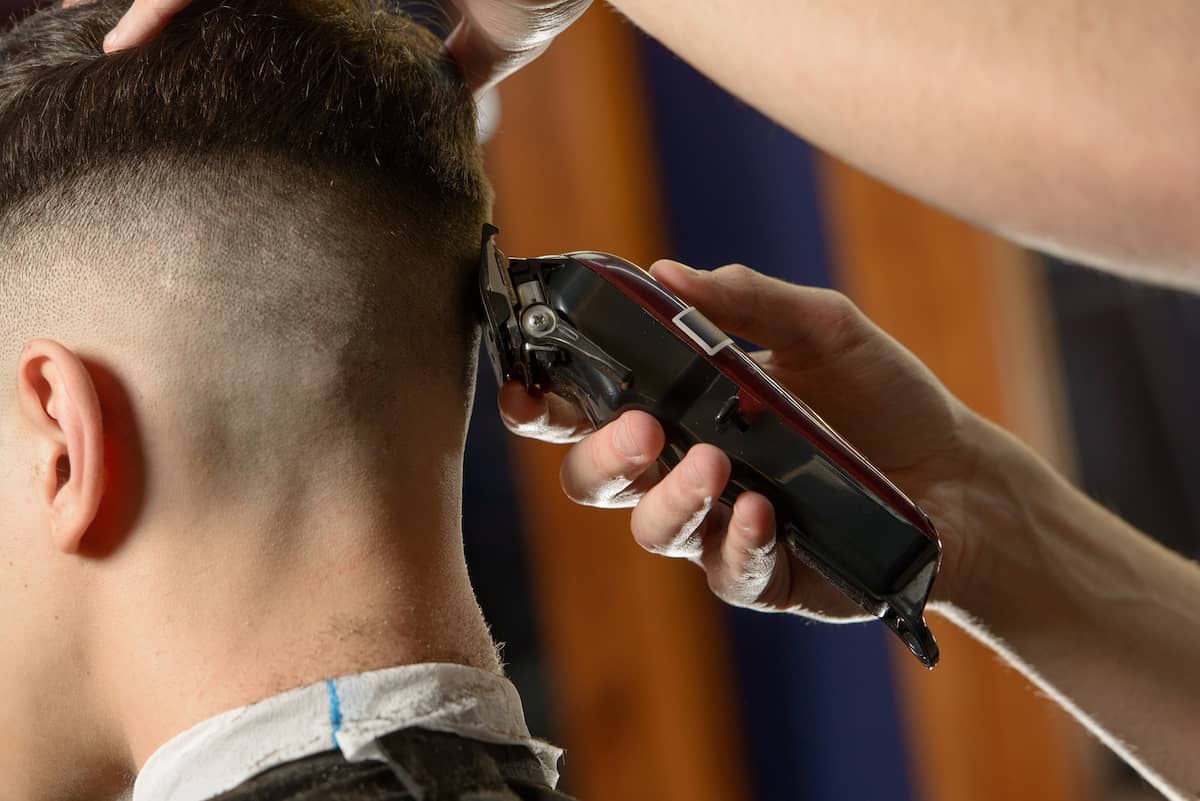 Nahaufnahme von einem Mann beim Frisör, dessen Haare für einen Boxerschnitt ausrasiert werden