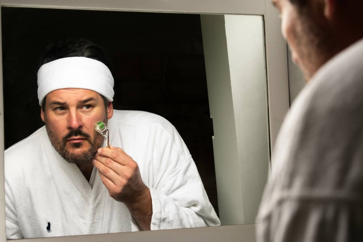 Mann rollt als Teil seiner Gesichtspflege für Männer mit einem Dermaroller über sein Gesicht