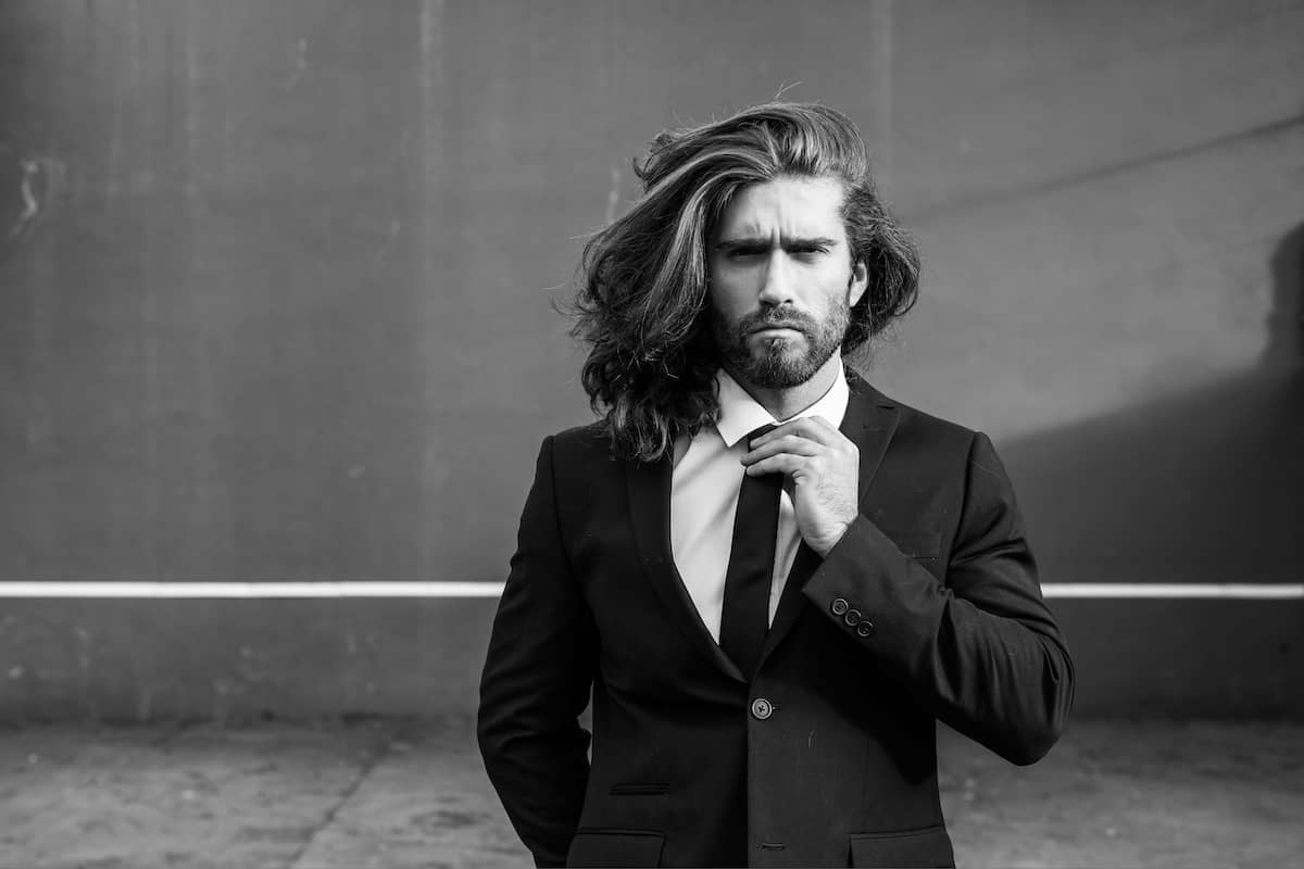 Langhaarfrisuren für Männer können auch im Business Look gut aussehen, wie dieser Mann mit langen Haaren und Anzug demonstriert