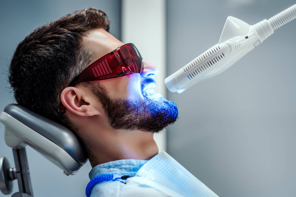 Mann erhält Zahnaufhellung mit UV Lampe beim Zahnarzt