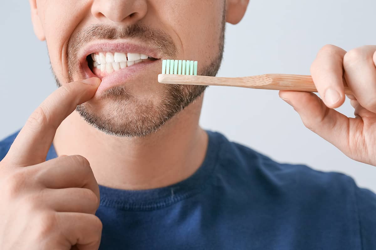 Mann mit Zahnimplantat hält Zahnbürste an den Mund