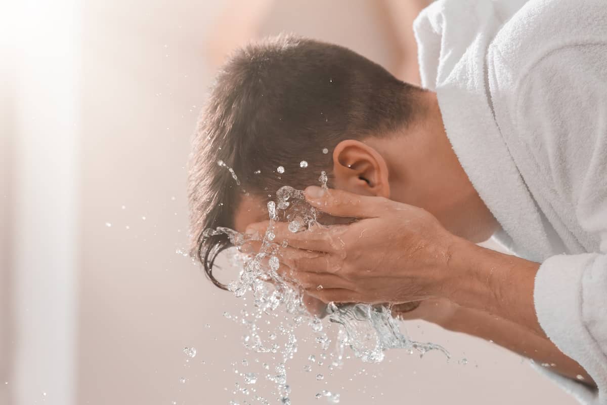 Mann wäscht seinen Dreitagebart mit Wasser am Waschbecken
