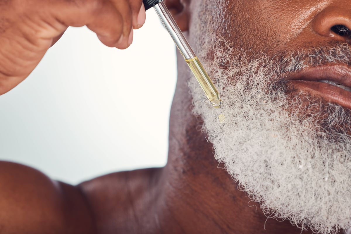 Mann mit grauem Bart tröpfelt Öl in seinen Bart 