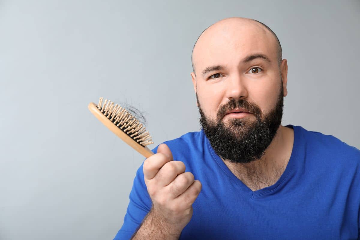 Mann mit Bürste voller Haare in der Hand 