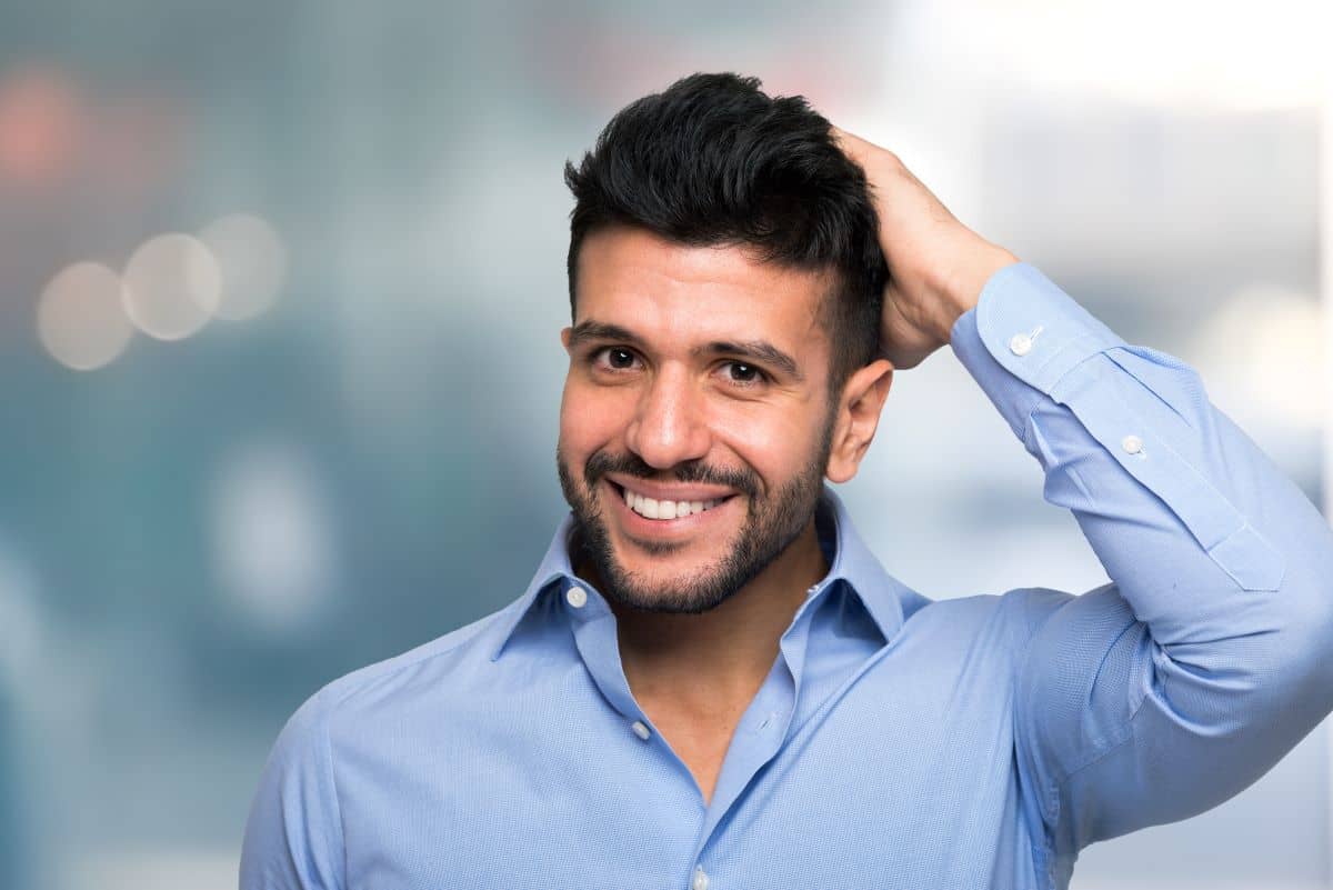 Erholung nach einer Haartransplantation - Mann mit schwarzen Haaren und blauem Hemd lächelt